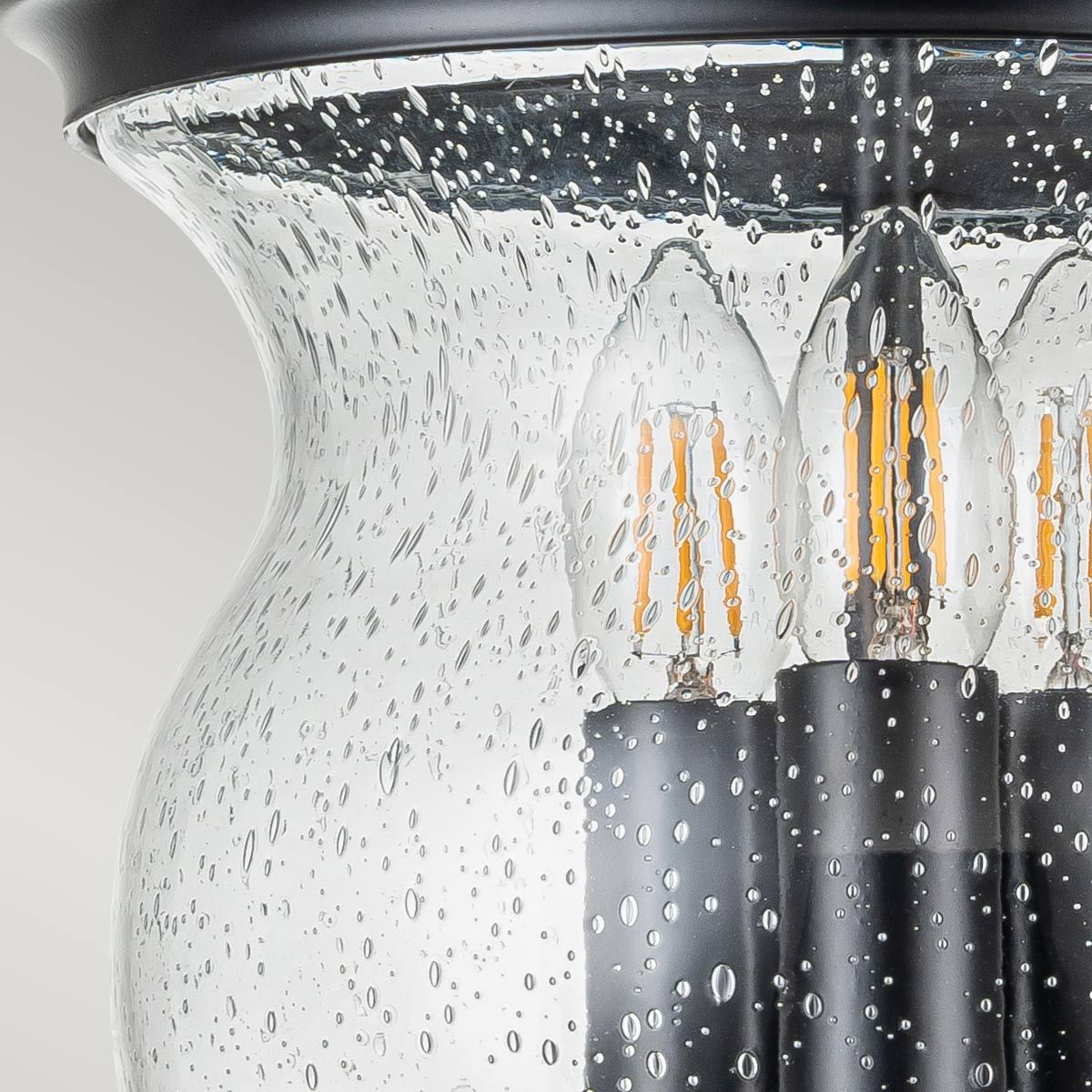 Lampa sufitowa Pickering z trzema gniazdami E14, w czarnej metalowej oprawie. Szklany klosz z fakturą bąbelków, odsłaniający żarówki z widocznymi włóknami. Ujęcie zbliżeniowe, podkreślające detale lampy.