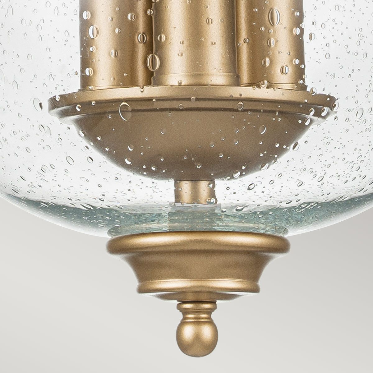 Lampa sufitowa Pickering 3xE14 w mosiężnym wykończeniu z przezroczystym kloszem z fakturą wody. Widoczny jest okrągły element mocujący z dekoracyjną kulką na dole. Klosz o zaokrąglonym kształcie.