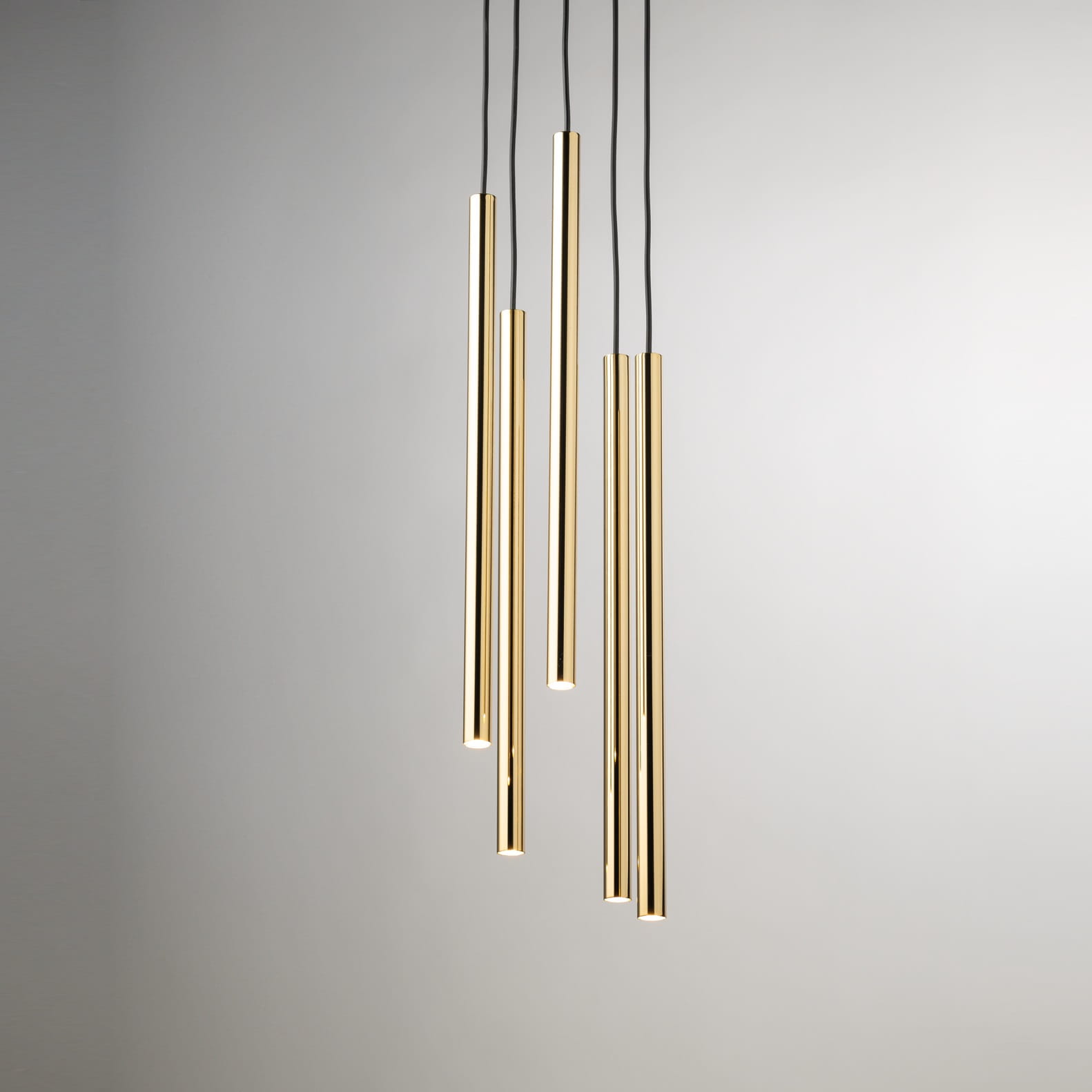 Lampa wisząca Sopel Lux z pięcioma złotymi rurkami G9. Rurki o różnych długościach zawieszone na czarnych przewodach, w minimalistycznym stylu. Tło jasne, jednolite, podkreślające elegancję lampy.