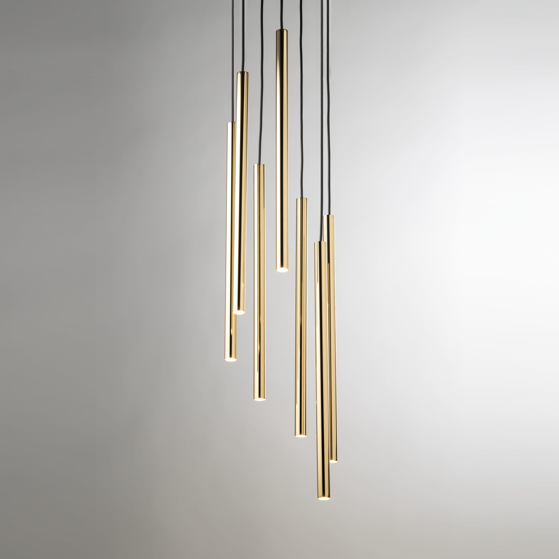 Lampa wisząca Sopel Lux z siedmioma prostokątnymi, złotymi kloszami na czarnych przewodach. Klosze różnej długości, zawieszone w dynamicznej aranżacji. Tło w kolorze jasnoszarym, podkreślające elegancję lampy.