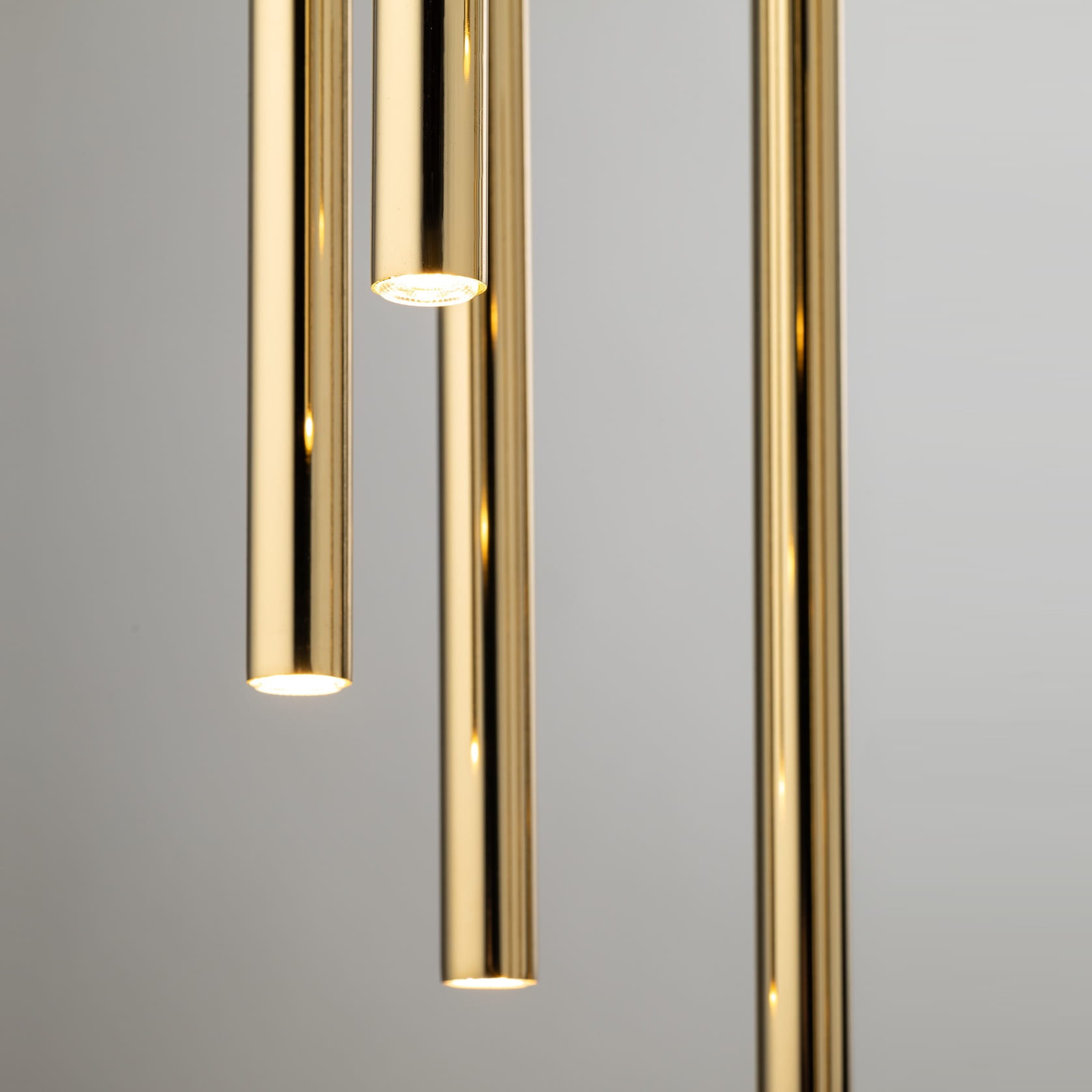 Lampa wisząca Sopel Lux w kolorze czarnym i złotym, składająca się z 7 cylindrycznych elementów. Zbliżenie na złote, błyszczące rurki z widocznymi źródłami światła na końcach. Tło w jasnym, neutralnym kolorze.