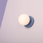 Kinkiet Ball II S w kolorze błękitnym, zamontowany na ścianie, z okrągłą, białą kloszem. Produkt widoczny z góry, prezentujący minimalistyczny design i gładką, matową powierzchnię.