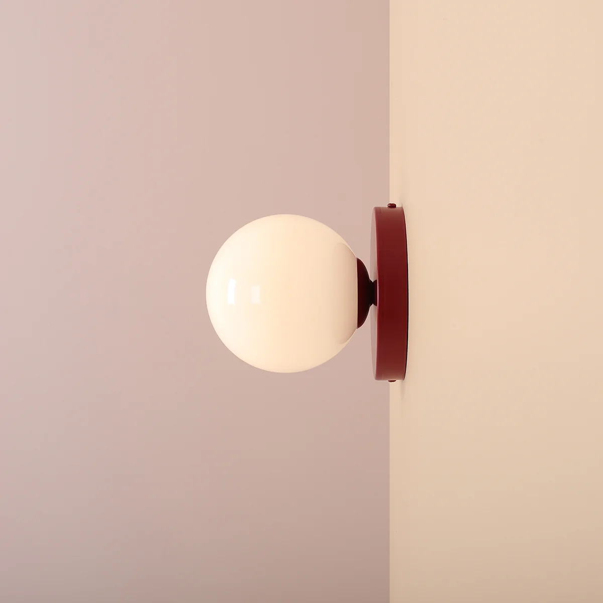 Kinkiet Ball II S w kolorze czerwonego wina z białą, okrągłą oprawą. Zamontowany na ścianie, w perspektywie bocznej, ukazuje gładką powierzchnię oraz minimalistyczny design. Idealny do nowoczesnych wnętrz.