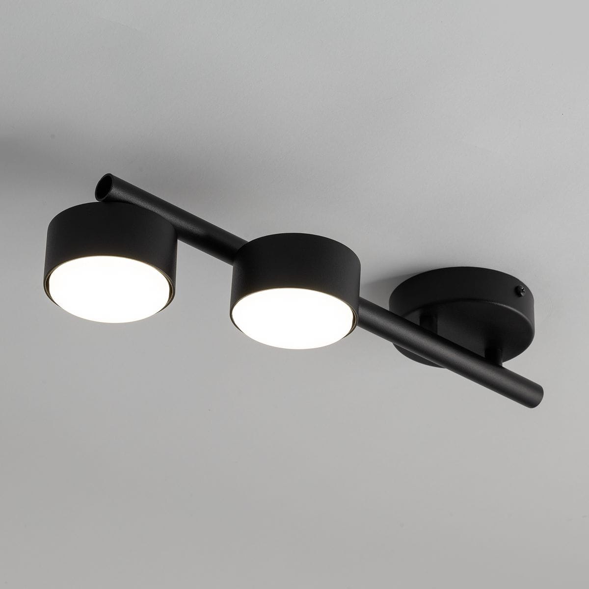 Lampa sufitowa Punto z dwoma okrągłymi źródłami światła w czarnej obudowie. Produkt zamontowany na okrągłej podstawie, z metalowym wspornikiem w poziomie. Widoczny matowy wykończenie oraz minimalistyczny design.