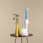 Lampa stołowa Ball Mustard z jedną oprawą E14, umieszczona na brązowym stoliku. W tle widoczna kolumna w białym kolorze z niebieskimi akcentami oraz wazon z suszonymi kwiatami i dwa okrągłe elementy – żółty i biały. Tło w odcieniu beżowym.