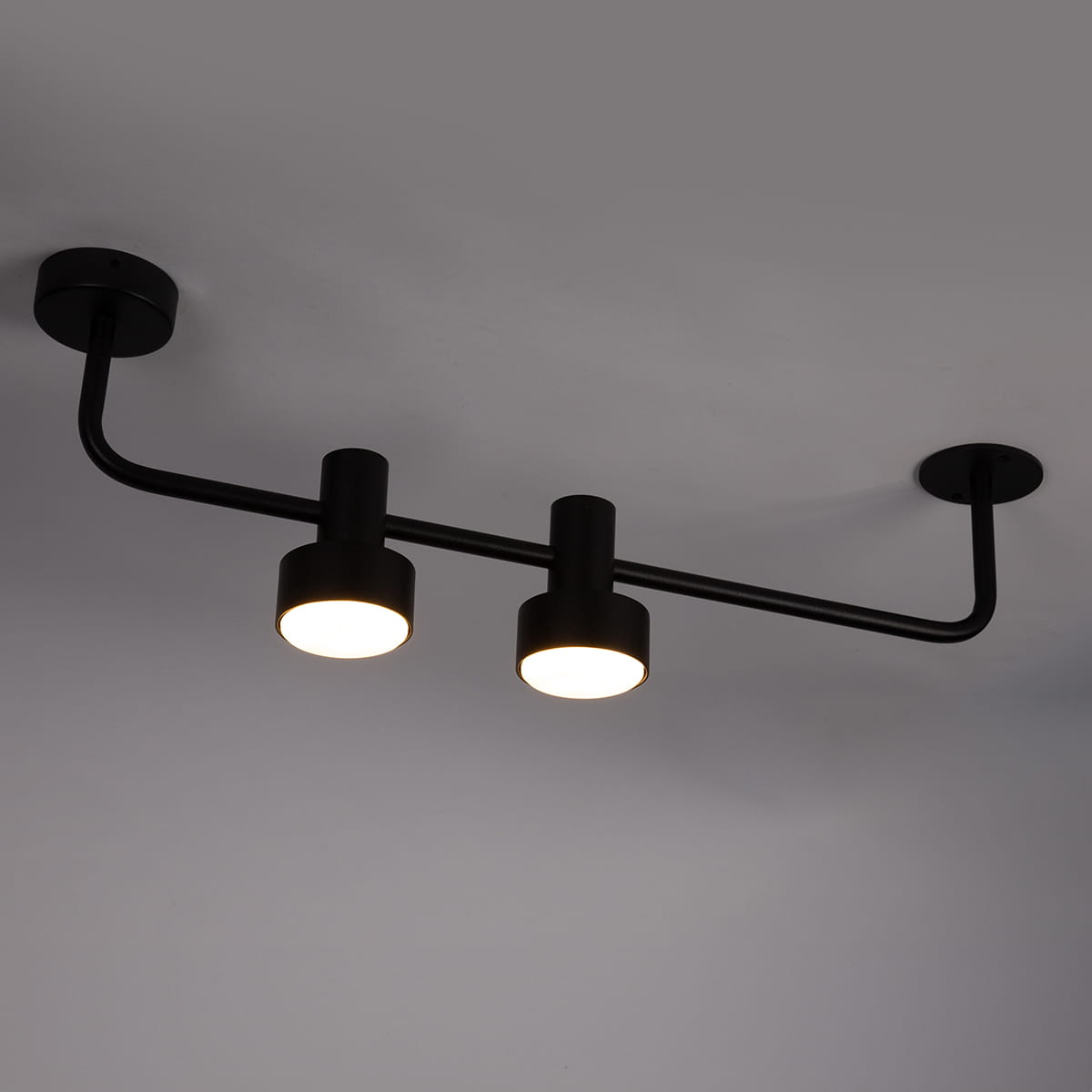 Lampa sufitowa Mona z dwoma źródłami światła GX53 w kolorze czarnym. Stylowy, prosty design z metalowym stelażem i zaokrąglonymi kloszami, zamontowana na suficie, z widocznym okablowaniem.