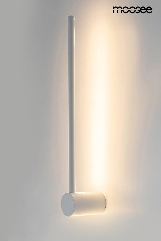 Kinkiet Ombre 60 LED w kolorze białym, o prostym, cylindrycznym kształcie. Posiada długi, wąski element świetlny w pionie oraz okrągłą podstawę. Oświetlenie emituje ciepłe światło, montowane na ścianie. Tło jasne, co podkreśla jego minimalistyczny design.