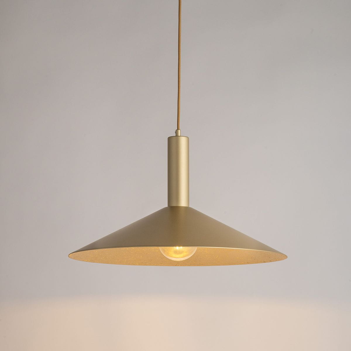 Lampa wisząca Capri D50 w kolorze złotym z metalowym kloszem w kształcie stożka. Wyposażona w jedno gniazdo E27 oraz widoczny żarówkę. Wisi na cienkim przewodzie, z prostym, minimalistycznym designem. Tło jasne, neutralne.