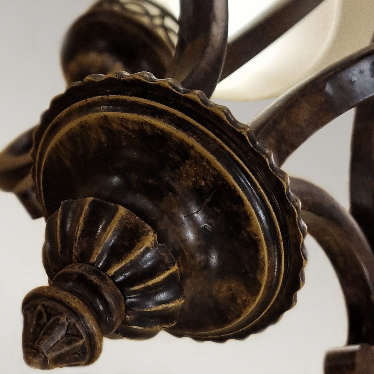 Lampa wisząca Drawing Room z czterema oprawami E27 w postarzanym brązie. Widoczne detale: ozdobna podstawa z falistą krawędzią i dekoracyjnym motywem w dolnej części. Ujęcie z dołu, ukazujące szczegóły konstrukcji.