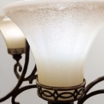 Lampa wisząca Drawing Room o postarzanym brązie z sześcioma kloszami E27. Klosze mają delikatną, matową teksturę, a ich kształt jest lekko rozszerzający się ku górze. Metalowa konstrukcja z dekoracyjnymi detalami w kolorze brązowym.