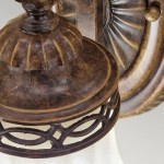 Kinkiet Drawing Room z postarzanym brązem, z kloszem w kształcie dzwonu. Widoczna dekoracyjna podstawa z geometrycznym wzorem oraz detale w kolorze brązowym. Ujęcie w zbliżeniu na górną część lampy i klosz.