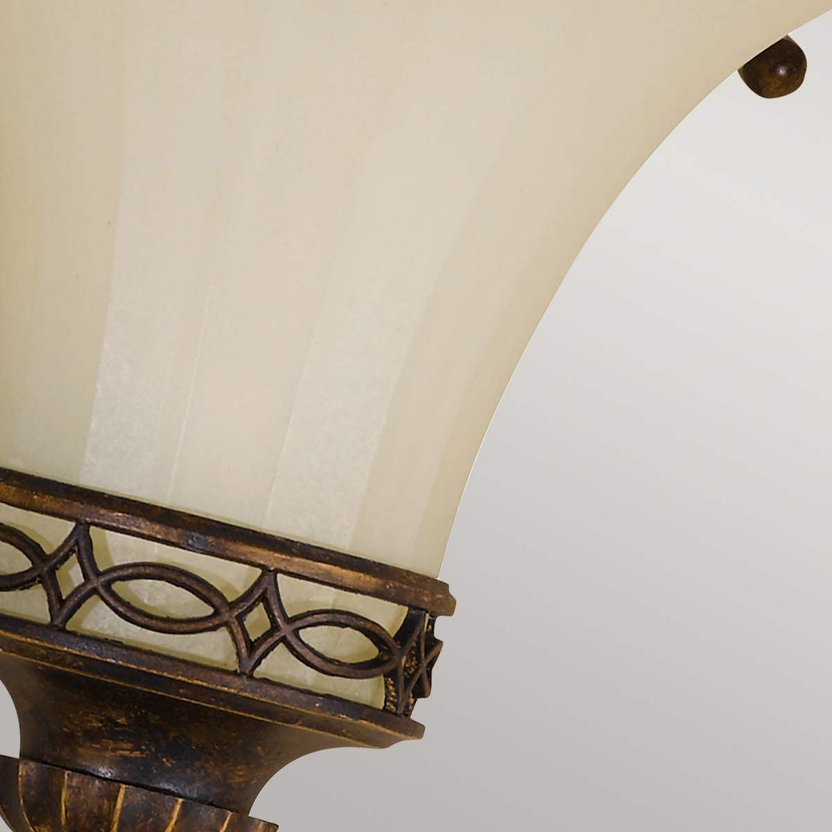 Kinkiet Drawing Room U 1xE14 w postarzanym brązie, z dekoracyjną oprawą i kloszem w kolorze kremowym. Ujęcie z boku, ukazujące szczegóły wzoru na metalowym elemencie oraz teksturę klosza.