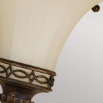 Kinkiet Drawing Room U 1xE14 w postarzanym brązie, z dekoracyjną oprawą i kloszem w kolorze kremowym. Ujęcie z boku, ukazujące szczegóły wzoru na metalowym elemencie oraz teksturę klosza.