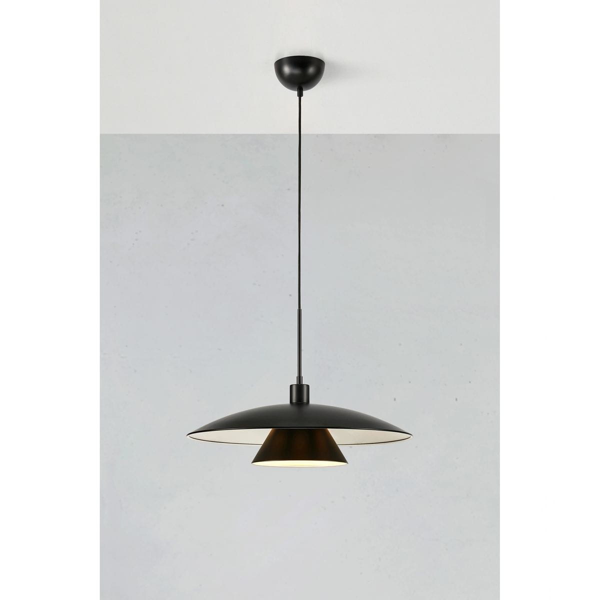 Lampa wisząca Millinge z jedną oprawą E27 w kolorze czarnym. Posiada stożkowaty klosz z zewnętrzną częścią w matowej czerni i wewnętrzną w złotym kolorze, zawieszona na cienkim kablu. Ujęcie z boku, na jednolitym tle.