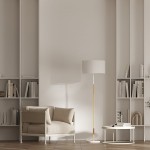 Biała lampa podłogowa Fogo z dwoma gniazdami E27, z metalowym stelażem w kolorze złotym. Lampa ma okrągły klosz, stojący na podłodze obok beżowej sofy w jasnym wnętrzu, na tle półek z książkami.
