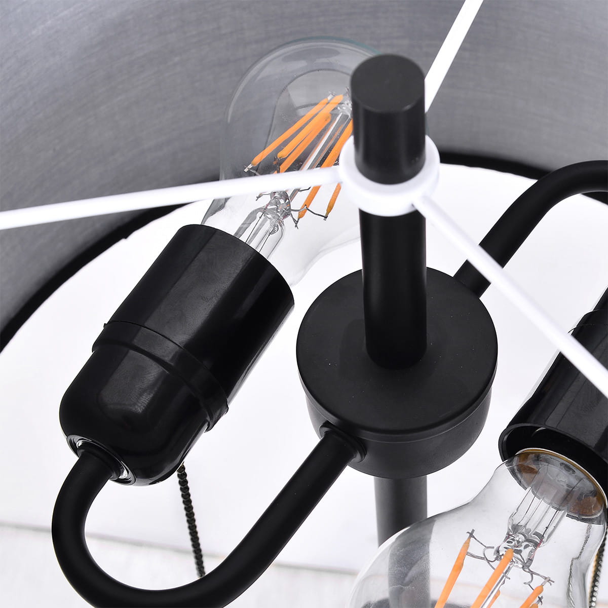 Lampa podłogowa Fogo w kolorze czarnym z dwoma gniazdami E27. Zbliżenie na elementy konstrukcyjne, w tym czarny uchwyt oraz przezroczyste żarówki z widocznymi włóknami. Prosta, nowoczesna forma z metalowym stelażem.