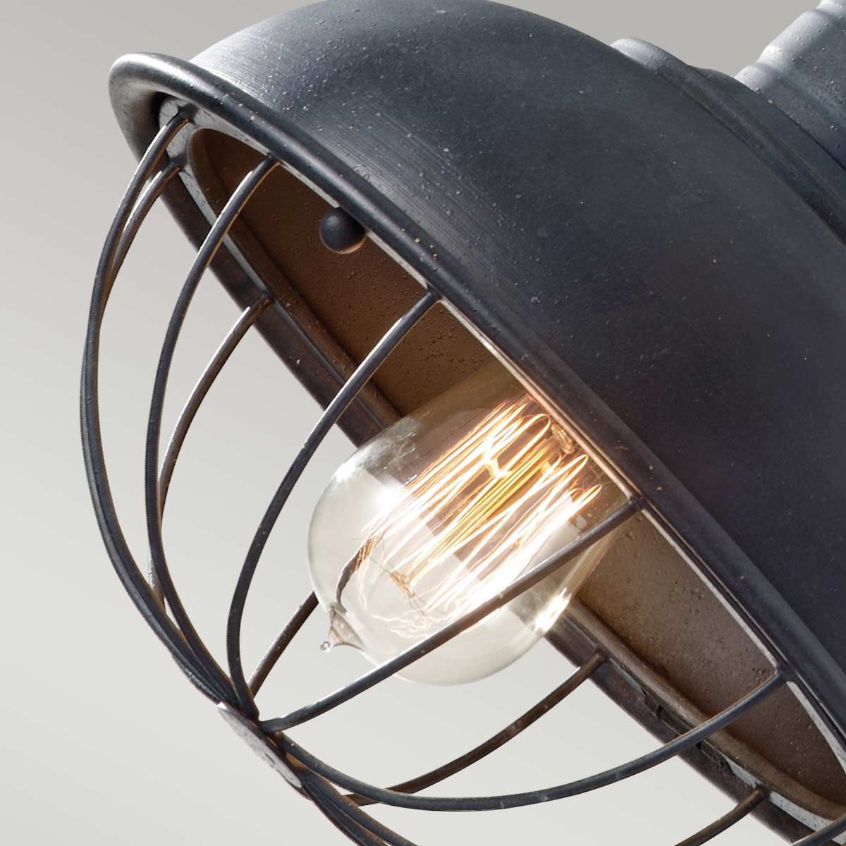 Lampa wisząca Urban Renewal z antycznego, kutego żelaza, z metalową osłoną w formie klatki. Widoczna żarówka E27 o szklanym kloszu, emitująca ciepłe światło. Ujęcie z góry, ukazujące detale konstrukcji oraz fakturę materiału.