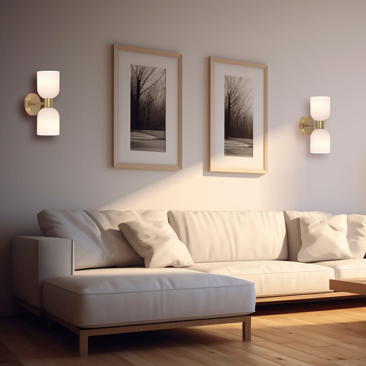 Kinkiet Piega 2xE14 w kolorze patynowym z białymi, żłobionymi kloszami, zamontowany na ścianie obok zdjęć w ramach. Produkt o nowoczesnym designie, umieszczony w aranżacji z jasną sofą i drewnianą podłogą.
