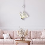 Lampa wisząca Mariposa w kształcie motyla, chromowana, z jedną żarówką LED o mocy 8W. Zawieszona nad różową sofą, w otoczeniu dekoracji roślinnych. Kąt ujęcia frontalny, na jasnym tle.