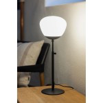 Lampa stołowa Rise H60 z podstawą w kolorze czarnym i kloszem w białym kolorze, z regulowaną wysokością, umieszczona na drewnianym stoliku. W tle widoczna kanapa z poduszką w jasnych odcieniach.