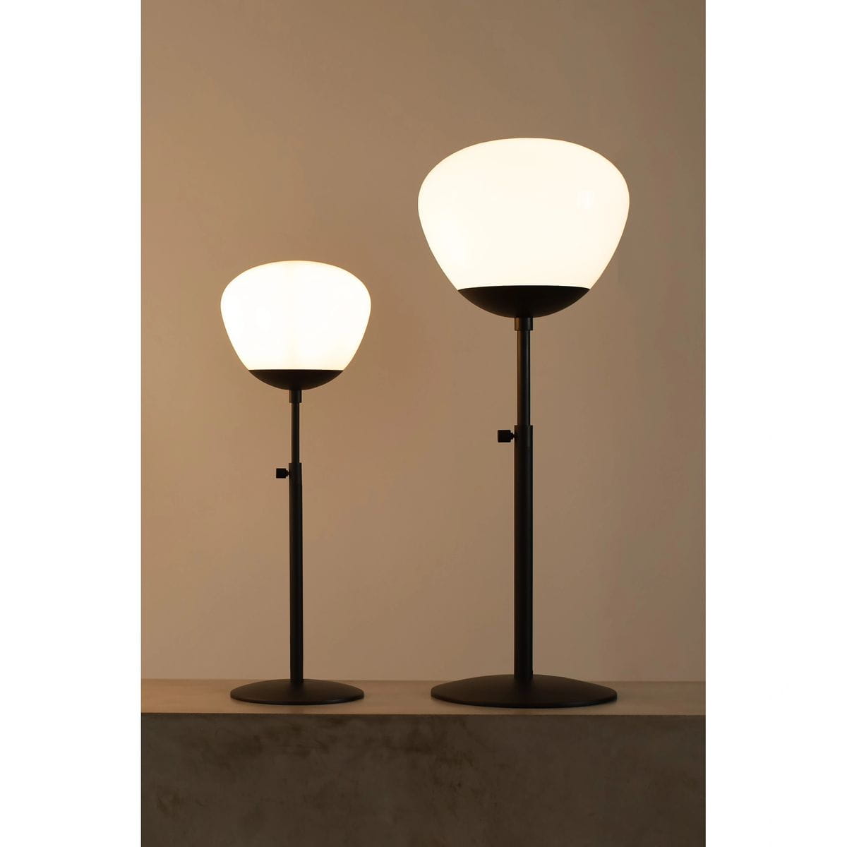 Lampa stołowa Rise H60 w kolorze czarnym i białym, z ceramiczną kloszem o zaokrąglonym kształcie. Widoczne dwie lampy o różnych wysokościach, stojące na płaskiej powierzchni. Metalowe podstawy zapewniają stabilność.