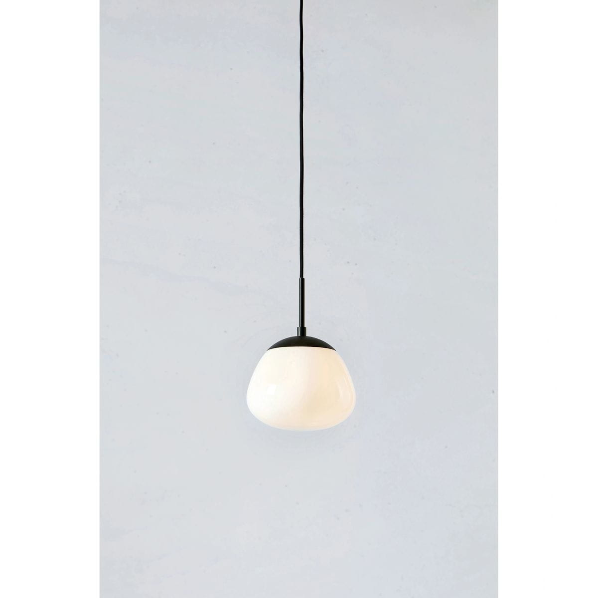 Lampa wisząca Rise D18 z oprawą w kolorze czarnym i białym, z okrągłym kloszem w kształcie kropli. Zawieszona na cienkim czarnym przewodzie, prezentuje minimalistyczny styl. Tło w jasnym odcieniu, podkreślającym elegancję lampy.