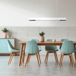Lampa wisząca Cali 80 w kolorze białym, z jedną żarówką LED o mocy 32W, zawieszona nad drewnianym stołem. W tle widoczne niebieskie krzesła oraz rośliny w doniczkach, na jasnym tle ściany.
