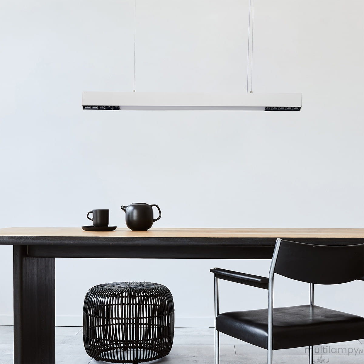 Lampa wisząca Cali 80 w kolorze białym, z jedną diodą LED o mocy 32W. Prosta, prostokątna forma, zawieszona na cienkich linkach, umieszczona nad drewnianym stołem, obok czarnych filiżanek i dzbanka, w minimalistycznym wnętrzu.