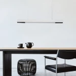 Lampa wisząca Cali 80 w kolorze białym, z jedną diodą LED o mocy 32W. Prosta, prostokątna forma, zawieszona na cienkich linkach, umieszczona nad drewnianym stołem, obok czarnych filiżanek i dzbanka, w minimalistycznym wnętrzu.