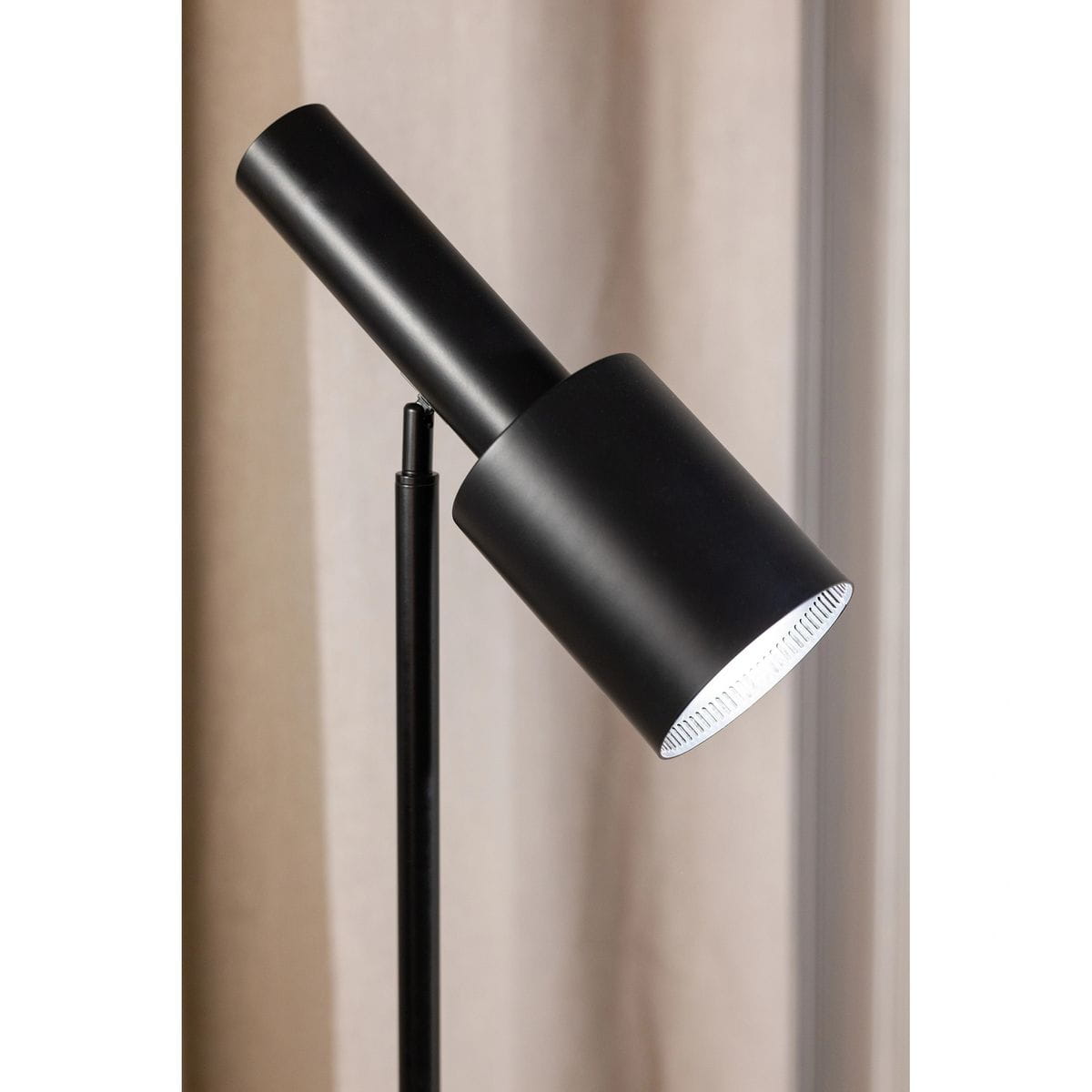 Czarna lampa podłogowa Ozzy z oprawą na żarówkę E27. Ujęcie z boku, ukazujące cylindryczną głowicę z metalowym wykończeniem i prostą, smukłą nogą. Tło w neutralnym kolorze, co podkreśla minimalistyczny design lampy.