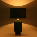Lampa stołowa Tamiza z butelkowo zielonym, teksturowanym kloszem i czarnym, okrągłym abażurem. Ujęcie frontalne, stojąca na okrągłej podstawie. Tło w odcieniach ciepłego beżu, podkreślające elegancki design.