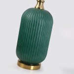 Lampa stołowa w butelkowej zieleni z wypukłymi prążkami, z metalową podstawą w kolorze złotym. Ujęcie z boku, pokazujące kształt owalny i detale tekstury. Idealna do nowoczesnych aranżacji wnętrz.