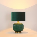 Lampa stołowa Tamiza w butelkowej zieleni z tekstylnym kloszem. Posiada złoty detal na podstawie i żłobioną, okrągłą formę. Ujęcie frontalne, lampa stoi na płaskiej powierzchni. Idealna do nowoczesnych aranżacji wnętrz.