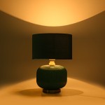 Lampa stołowa w butelkowej zieleni z ceramiczną podstawą o żłobionej fakturze i czarnym abażurem. Ujęcie z przodu, stojąca na okrągłej podstawie, emituje ciepłe światło, podkreślając elegancki design.