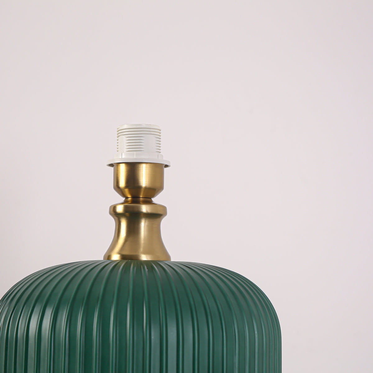 Lampa stołowa w butelkowej zieleni z podstawa w kolorze złotym, z widocznym gniazdem na żarówkę E27. Uformowana w kształcie cylindrycznym z poziomymi wgłębieniami, stojąca na płaskiej powierzchni, na jasnym tle.