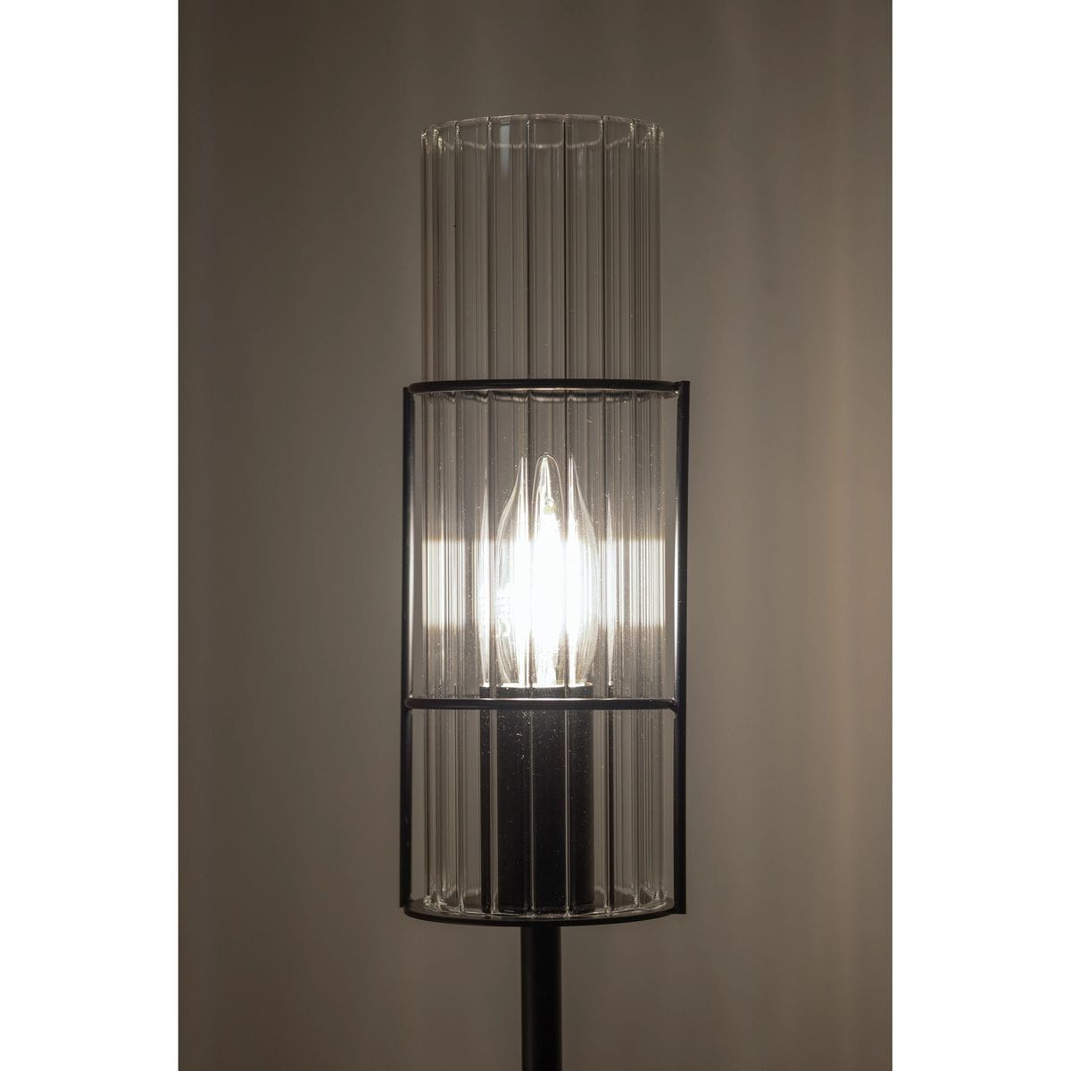 Lampa stołowa Tubo H65 z podstawką w kolorze czarnym i przeźroczystym kloszem z pionowymi żłobieniami. Ujęcie frontalne, z widoczną żarówką E14 wewnątrz. Tło jasne i jednolite, podkreślające design lampy.