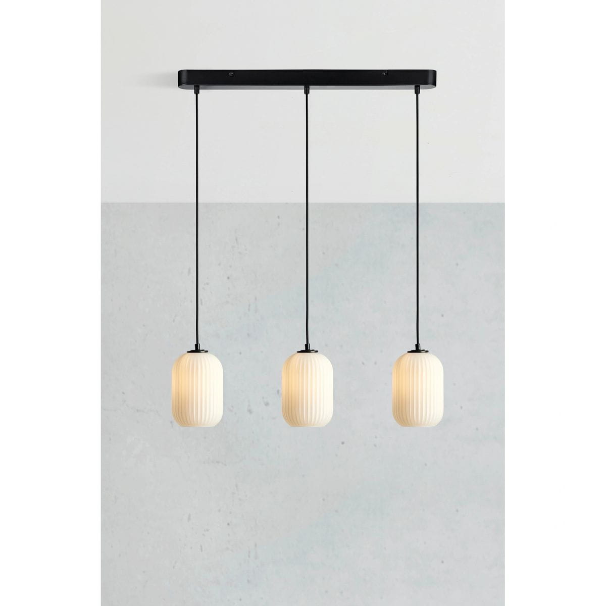 Cava lampa wisząca 3xE14 w kolorze czarnym i białym, z trzema cylindrycznymi kloszami o fakturze żłobkowanej, zawieszona na czarnym stelażu. Klosze w białym kolorze, umieszczone na długich przewodach, tworzą nowoczesny design.