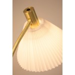 Lampa podłogowa Mira z kloszem w białym kolorze, wykonana z plisowanego materiału. Szczotkowany mosiądz na podstawie i ramieniu. Widok z góry, skupiony na detalu mocowania i klosza. Przycisk włącznika u góry.
