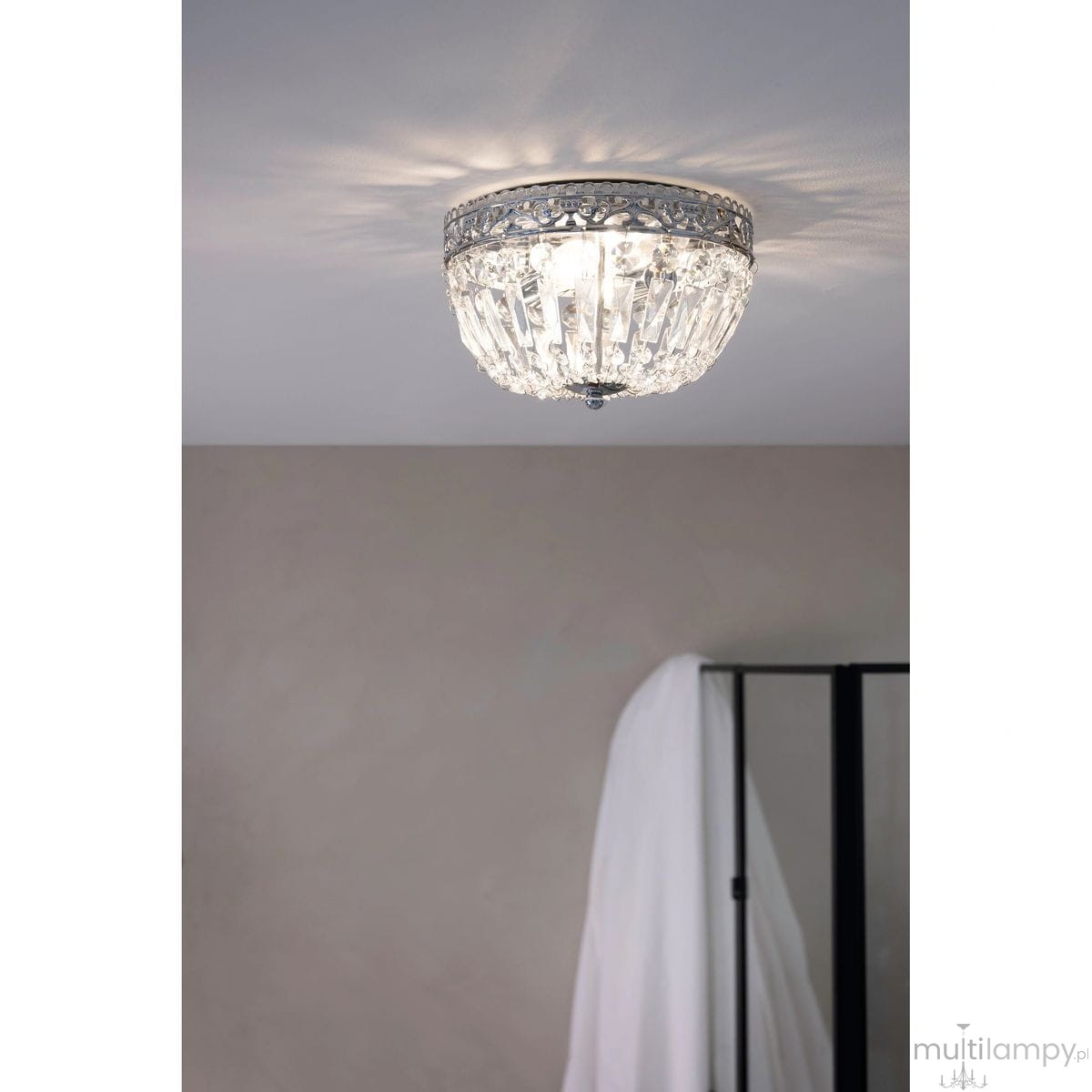 Lampa sufitowa Etienne z chromowanym wykończeniem, z dwiema oprawami E14. Okrągła konstrukcja z przezroczystymi kryształkami, montowana na suficie, emitująca miękkie światło w neutralnym wnętrzu. Widoczny fragment ściany w tle.