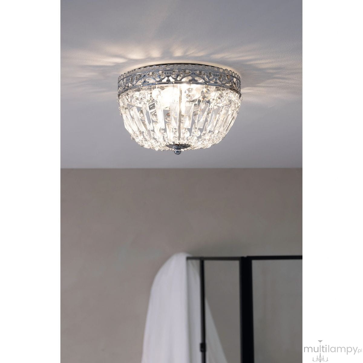 Lampa sufitowa Etienne w kolorze chromu, z dwoma gniazdami E14. Okrągła, z kryształowymi elementami, zamontowana na suficie. Wytwarza efektowne refleksy świetlne, idealna do nowoczesnych wnętrz. Tło w neutralnym odcieniu.