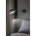 Kinkiet Portland 1xE27 w chromowanym wykończeniu, z okrągłą, błyszczącą czaszą. Lampa zamontowana na ścianie obok szarej kanapy z poduszką. Widoczny zintegrowany kabel. Tło w odcieniach szarości, tworzy elegancką aranżację.