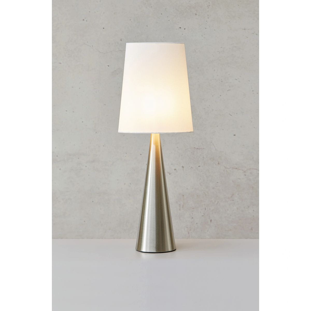 Lampa stołowa Conus z niklowanym, satynowym trzonem w kształcie stożka oraz białym abażurem. Ujęcie frontalne, lampa stojąca na jednolitym tle. Przeznaczenie: oświetlenie wnętrz. Wysoka, nowoczesna forma.