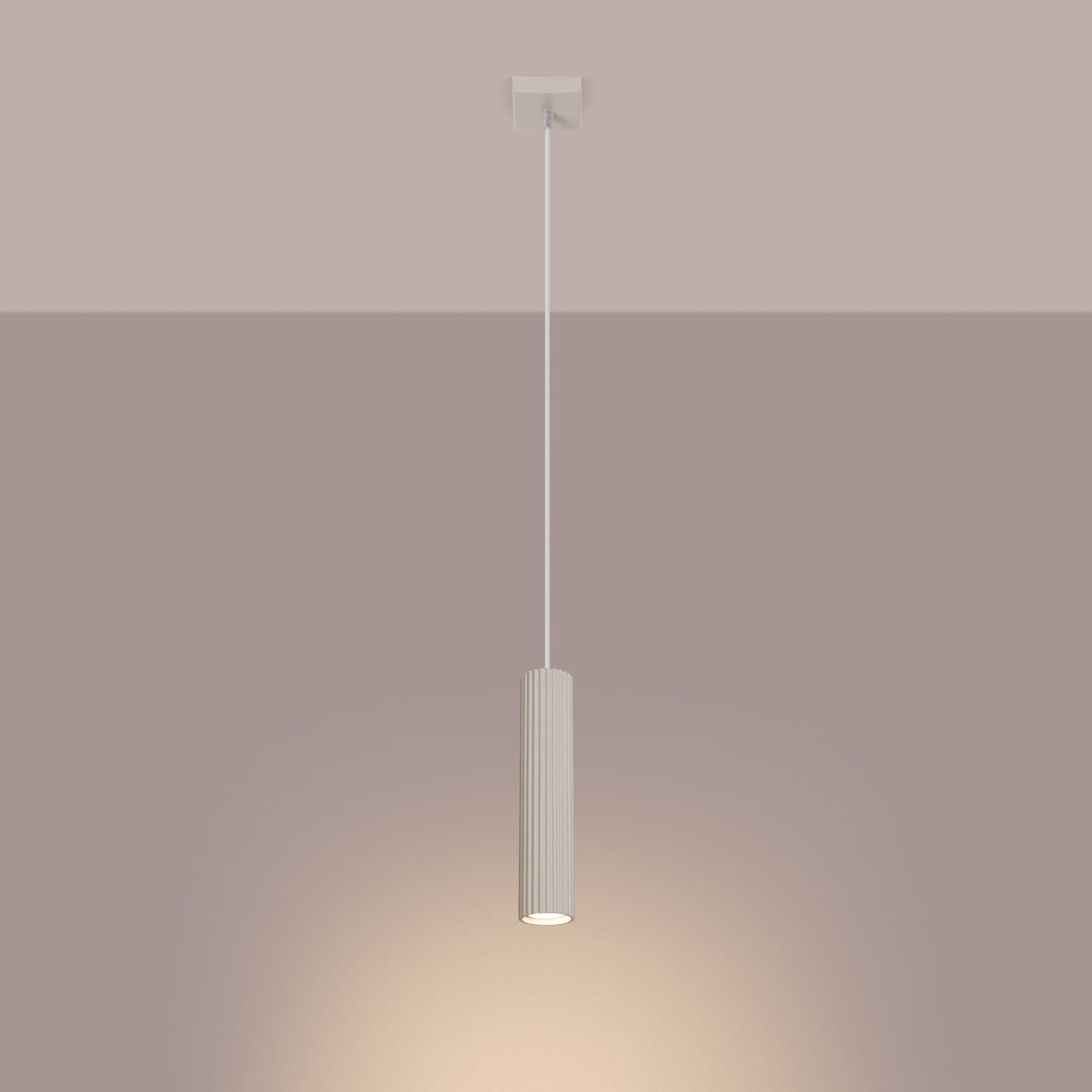 Beżowa lampa wisząca Karbon 1 z jednym gniazdem GU10, o cylindrycznym kształcie z pionowymi żłobieniami. Zawieszona na cienkim, białym przewodzie, emitująca ciepłe światło w jednolitym, stonowanym tle.