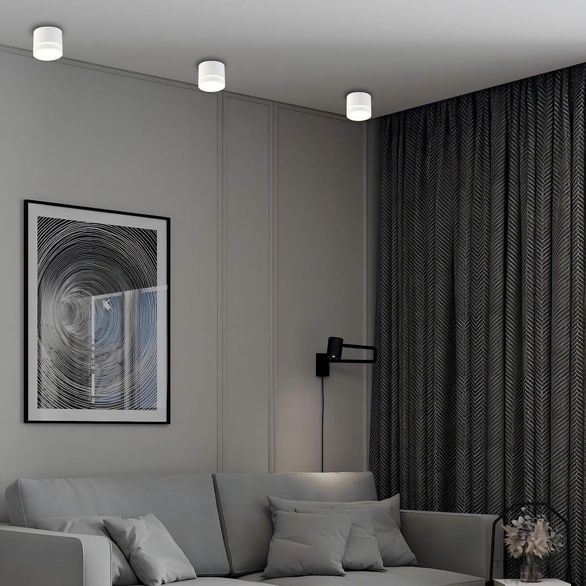 Lampa sufitowa Kendal 1xGX53 w kolorze białym, zamontowana na suficie. Okrągły kształt, matowa powierzchnia. W tle widoczna szara ściana, zasłony z wzorem oraz kanapa z poduszkami.