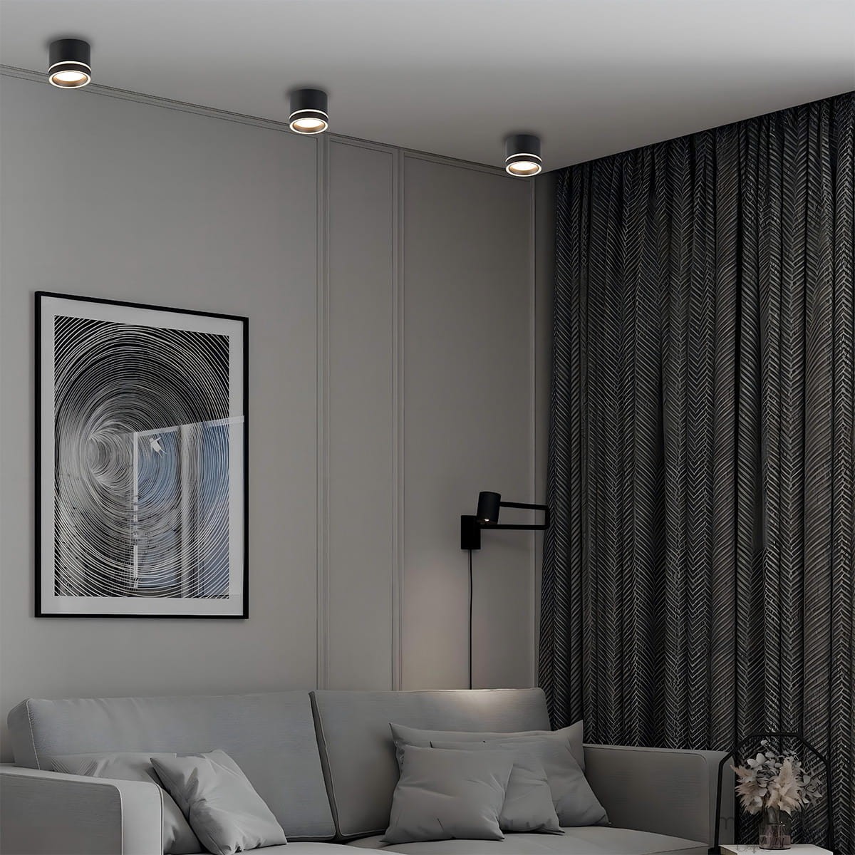 Czarna lampa sufitowa Kendal (spot) 1xGX53 z ruchomą głowicą, zamontowana na białym suficie. W tle widoczna szara sofa z poduszkami oraz ciemne zasłony z wzorem. Obok obraz w ramie z abstrakcyjnym motywem.