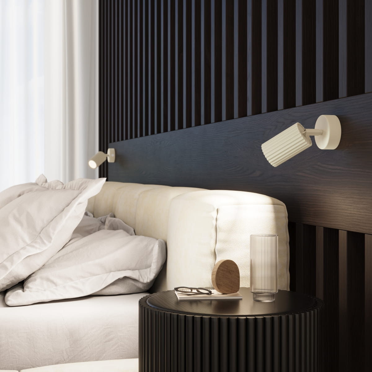 Kinkiet Karbon w kolorze beżowym z włącznikiem, zamontowany na drewnianej ścianie, skierowany w stronę łóżka. W tle widoczne poduszki oraz okrągły stolik z dekoracjami.