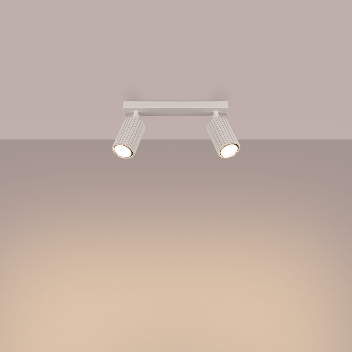 Beżowa lampa sufitowa typu spot z dwoma oprawami GU10, umieszczona na prostokątnej podstawie. Reflektory o fakturze żłobionej, skierowane w różnych kierunkach, montowane na suficie. Tło w delikatnym odcieniu beżu.
