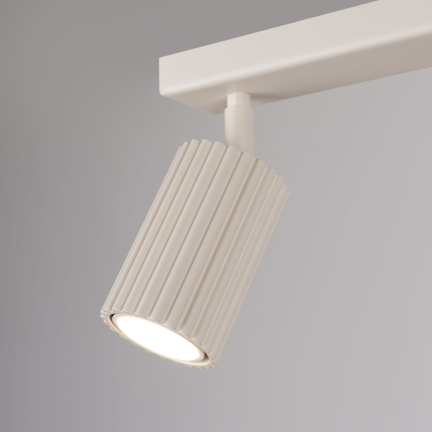 Beżowa lampa sufitowa typu spot z dwoma oprawami GU10. Cylindryczny klosz w fakturze żłobionej, zamontowany na prostokątnej podstawie. Ujęcie w zbliżeniu, ukazujące detal klosza i jego kształt. Tło w jasnym odcieniu.