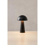 Czarna lampa stołowa akumulatorowa Fungi, z kształtem grzyba. Posiada okrągły klosz i stożkowaty trzon. Widoczna dioda LED emitująca ciepłe światło. Ustawiona na drewnianym stole, na tle gładkiej, jasnej ściany.