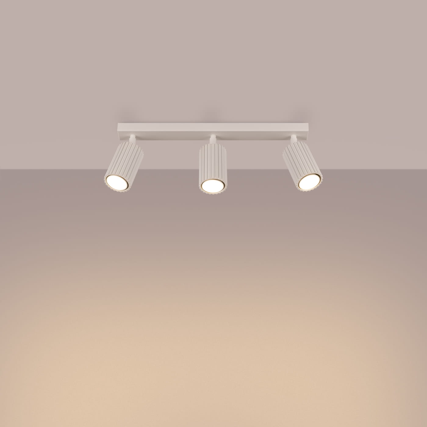 Beżowa lampa sufitowa typu spot z trzema oprawami na żarówki GU10. Ułożona poziomo, z widocznymi żarówkami w cylindrycznych, żebrowanych kloszach. Tło w jasnym kolorze, podkreślające minimalistyczny design lampy.